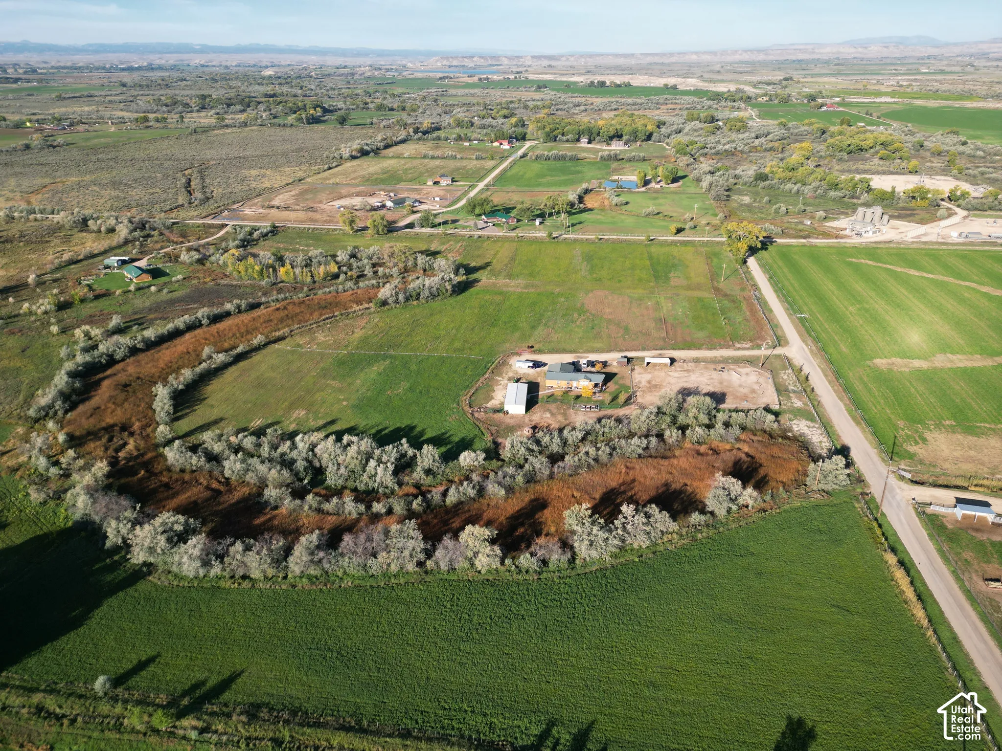 Expansive green fields, winding natural waterway, and distant mountain backdrop
