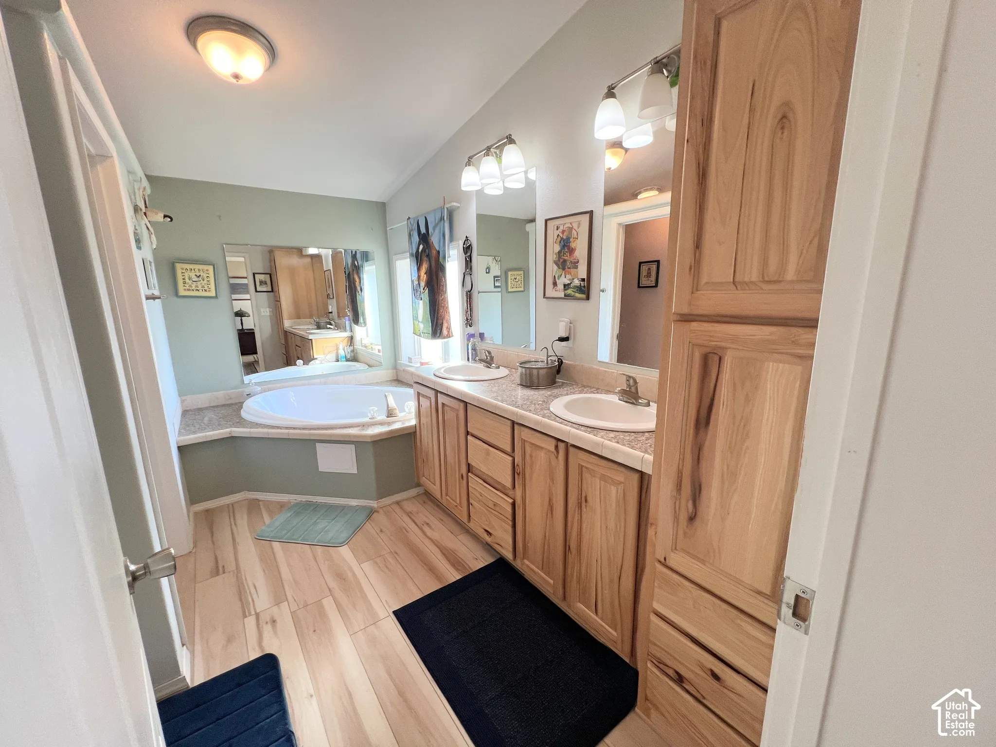 Dual vanity with integrated sinks, built-in soaking tub, wood-finish flooring, and natural wood cabinetry