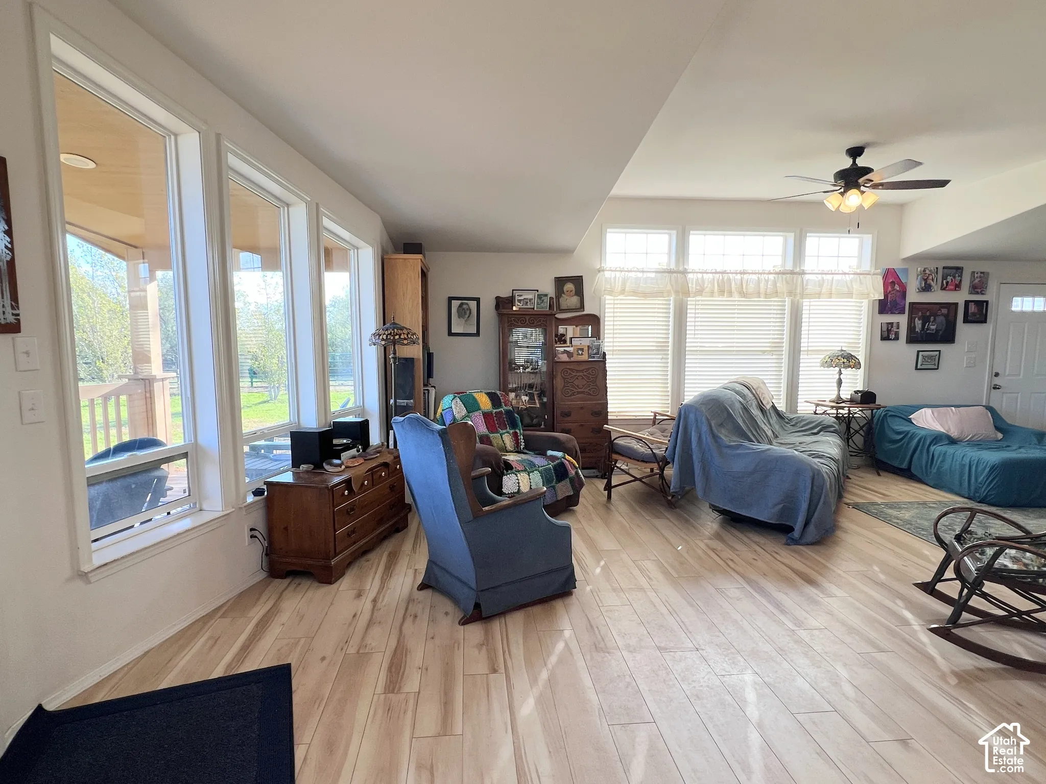 Spacious living area featuring light wood-finish flooring, multiple large windows, a ceiling fan, and a light-colored ceiling