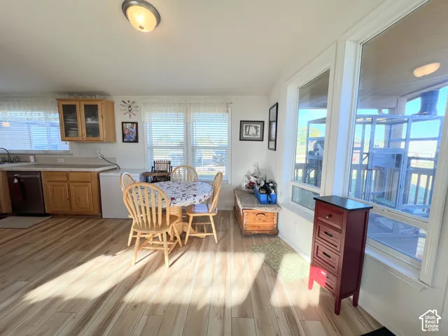 Wood-finish flooring, light wood cabinetry with glass-front uppers, stainless steel dishwasher, and multiple windows with white trim