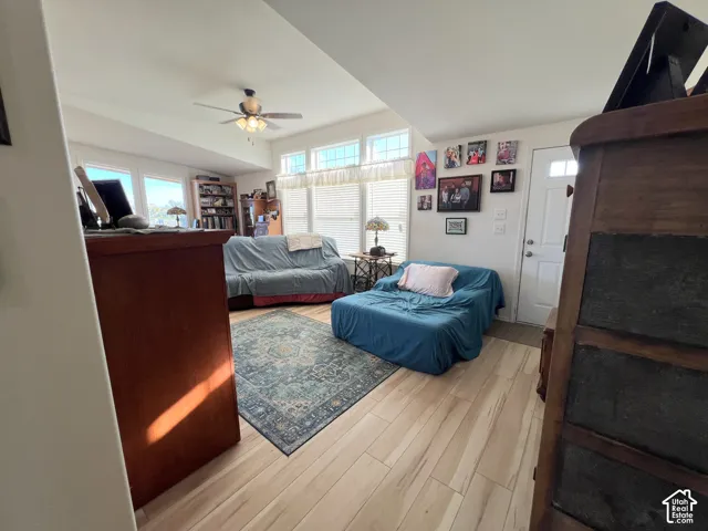 Wood-finish flooring throughout, ceiling fan with integrated lighting, and multiple windows with horizontal blinds
