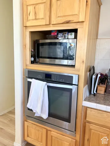 Built-in stainless steel oven, integrated microwave, light wood-finish cabinetry, and a tile countertop