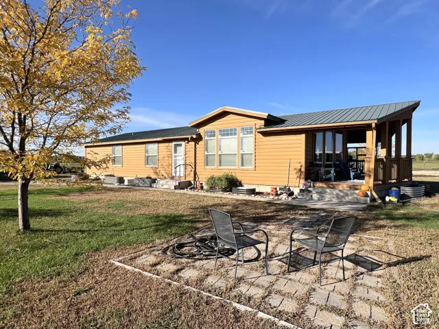 Exterior siding in a natural wood tone, covered porch with wood railing, metal roof, and a patterned paver patio