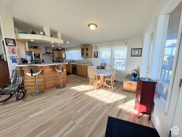 Kitchen featuring wood-finish flooring, light wood cabinetry, stainless steel appliances, and a breakfast bar with a paneled wood front