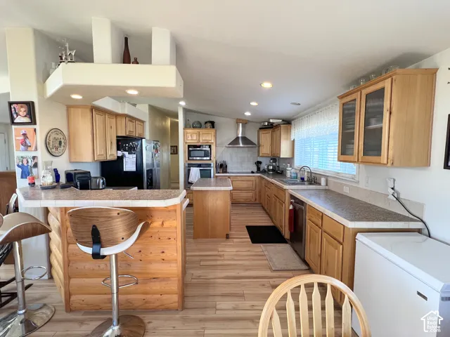 Kitchen featuring wood-finish flooring, natural wood cabinetry, a built-in breakfast bar with log-style detailing, recessed lighting, and a stainless steel range hood