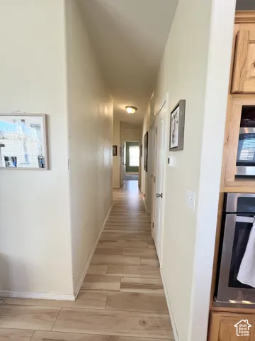 Wood-finish tile flooring throughout the hallway, featuring light-toned walls and built-in cabinetry with stainless steel appliances