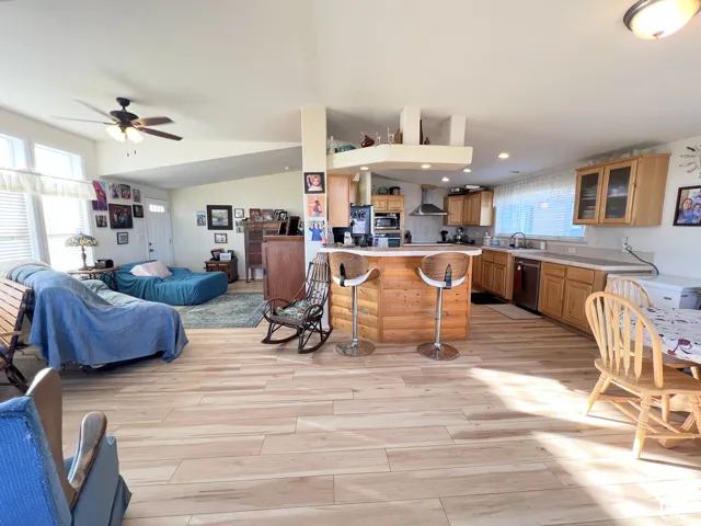 Open-concept living space featuring wood-finish flooring, a kitchen island with seating, natural wood cabinetry, and a ceiling fan