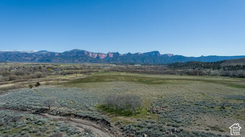 Expansive natural landscape featuring varied terrain, a dry creek bed, and distant mountain ranges