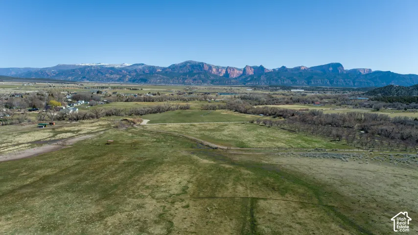 Expansive green fields with a distant mountain range featuring snow-capped peaks and red rock formations