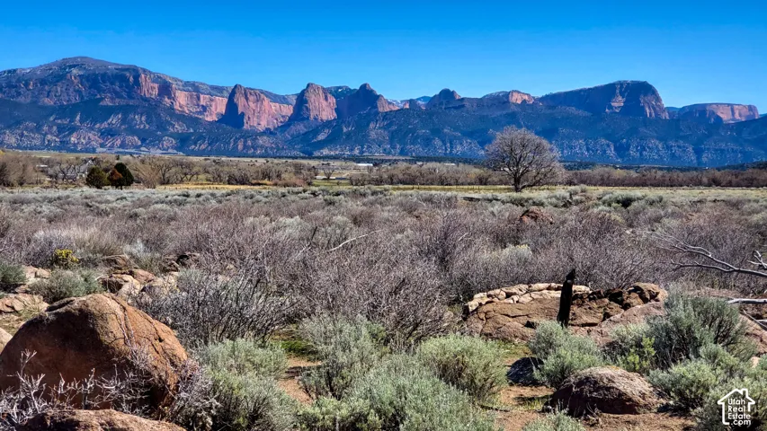 Mountain backdrop with clear blue sky, featuring a expansive natural landscape with scattered brush and visible rock formations