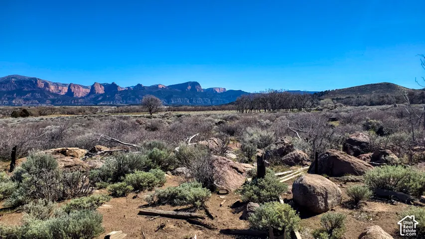 Expansive desert landscape with natural rock formations, scattered brush, and distant mountain ranges under a clear sky