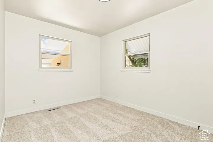 Light-colored walls, patterned carpet flooring, and two windows with white trim
