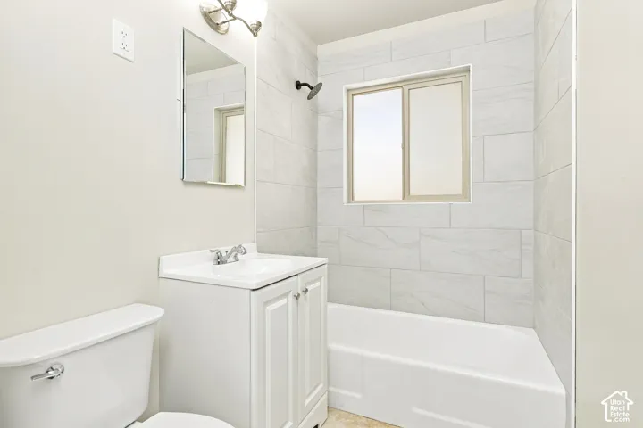 Bathroom featuring a window, white subway tile shower surround, white vanity with cabinet storage, and a chrome faucet