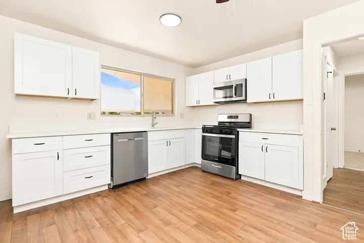 Kitchen featuring white cabinetry, light-toned countertops, wood-finish flooring, stainless steel appliances, and a window