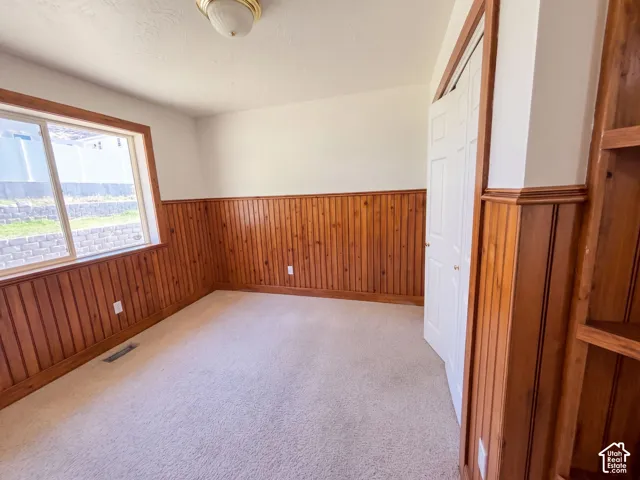 Wood paneling, neutral carpeting, window with wood trim, white bi-fold closet doors, built-in wooden shelving