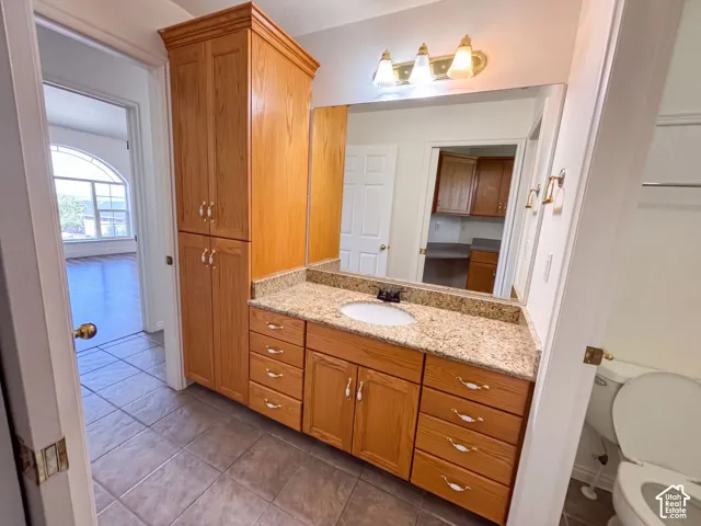 Vanity with an integrated sink, granite-style countertop, wood-finish cabinetry, and tiled flooring