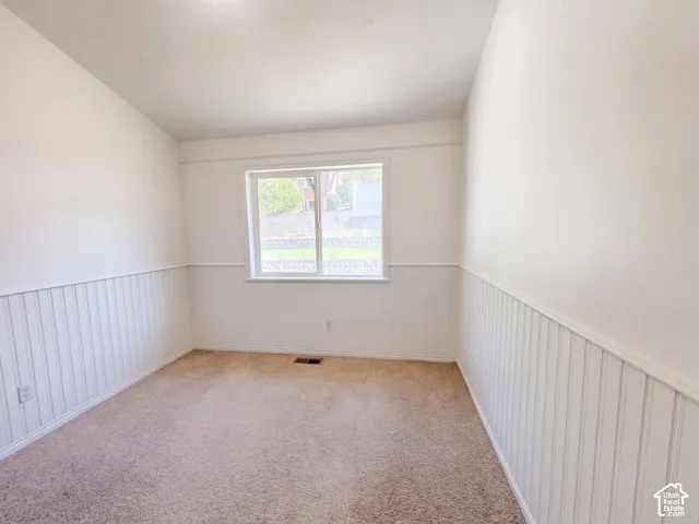 Light-colored carpeting, white wainscoting, and a window with a white frame