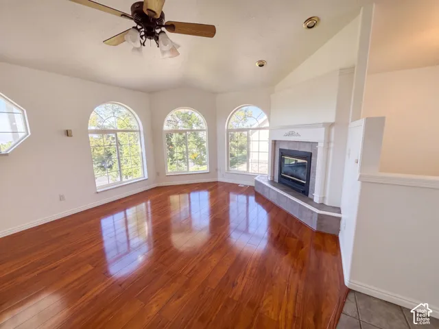 Vaulted ceiling with a ceiling fan, arched windows, wood-finish flooring, and a fireplace with a tile hearth