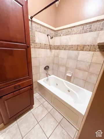 Integrated soaking tub with shower, full-height tiled surround with mosaic accent, built-in wood cabinetry, and tile flooring