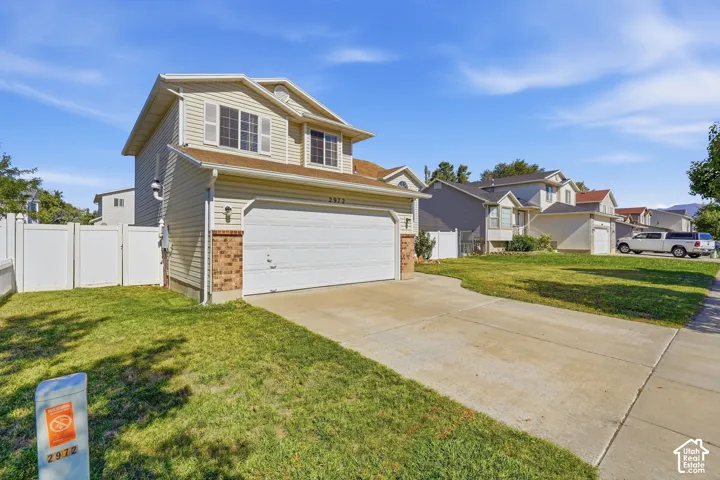 Two-story property with horizontal siding, an attached two-car garage, partial brick facade, and a white picket fence