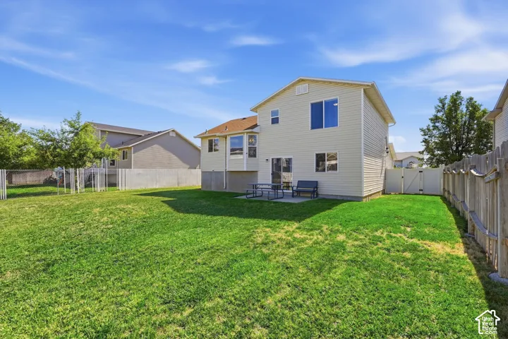 Expansive grassy yard with full fencing, a concrete patio, and a side access gate