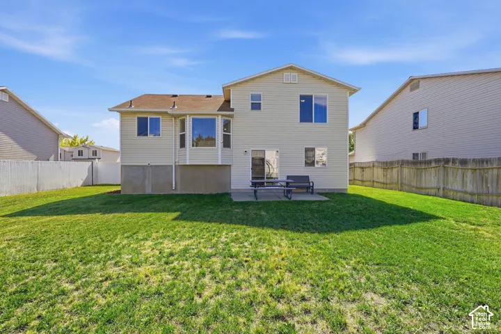 Expansive green yard with a concrete patio, featuring a bay window, sliding glass door, and a white privacy fence
