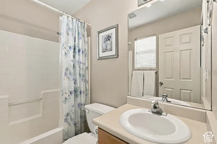 White tile tub/shower combination, single vanity with integrated sink, and wood-finish cabinetry