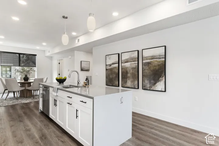 Kitchen island with integrated sink, stainless steel dishwasher, white shaker-style cabinetry, and light-toned countertop Pictures are of the model home