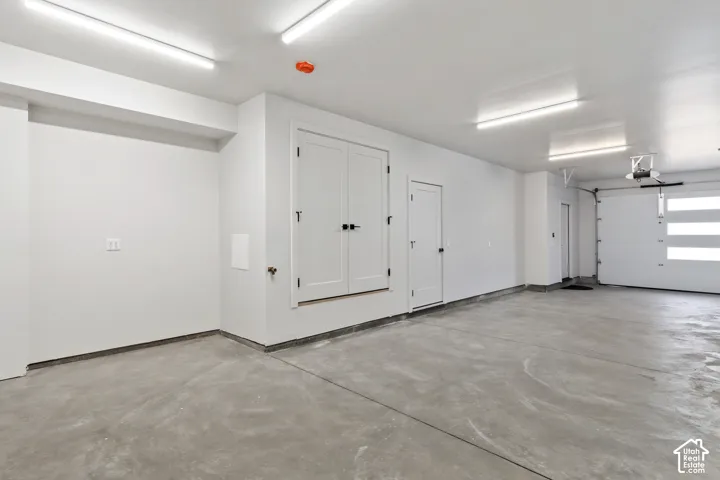 Spacious garage featuring a concrete floor, overhead lighting, an overhead door with horizontal frosted glass panels, and built-in storage with double doors