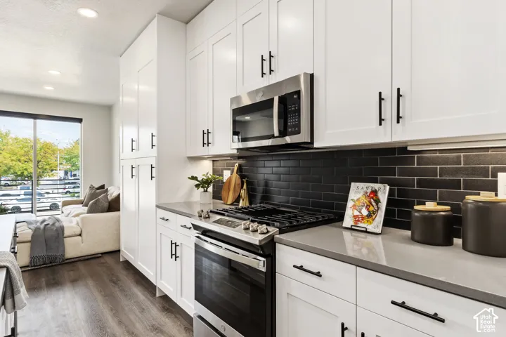 Modern kitchen featuring white shaker cabinetry, stainless steel appliances, dark subway tile backsplash, light stone countertops, and wood-finish flooring Pictures are of the model home