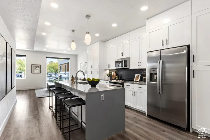 Open-concept kitchen with white shaker cabinetry, stainless steel appliances, a dark subway tile backsplash, and a multi-level island with a light-toned countertop Pictures are of the model home