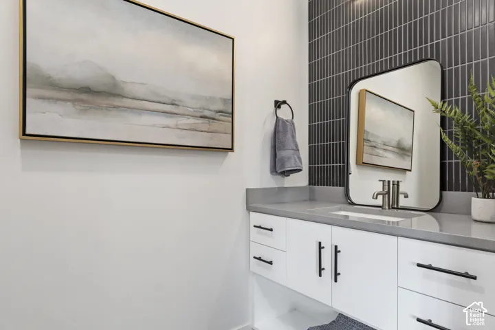 White vanity with black hardware, integrated rectangular sink, gray countertop, black framed mirror, and dark vertical tile accent wall Pictures are of the model home