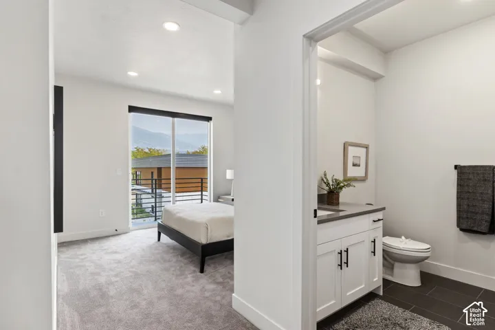 Bright interior with recessed lighting, sliding glass door, mountain scenery, and a bathroom featuring a white vanity with black hardware and a dark tile floor Pictures are of the model home