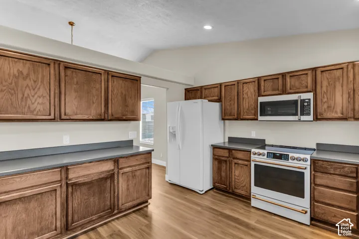 Kitchen featuring wood-finish cabinetry, solid surface countertops, LVP flooring, and white appliances including a refrigerator, range, and microwave