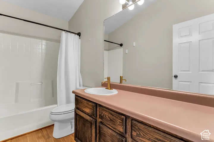 White tile surround bathtub, wood-finish flooring, vanity with wood-finish cabinetry, integrated sink, and wall-mounted mirror