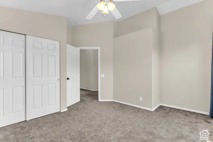 Vaulted ceiling with an attached ceiling fan, neutral tone wall paint, paneled interior doors, and grey carpeting