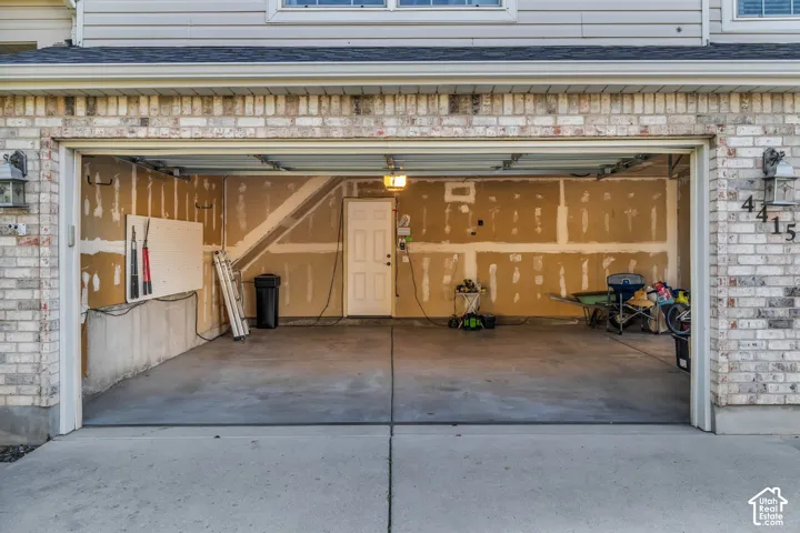 Attached three-car garage with a concrete floor, brick exterior, and permanent exterior lighting fixtures