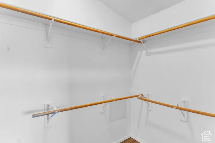 Walk in closet, white wall finishes, multiple wood-finish hanging rods, and built-in shelving brackets