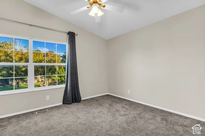 Vaulted ceiling with a ceiling fan light fixture, large paneled window, and wall-to-wall carpeting
