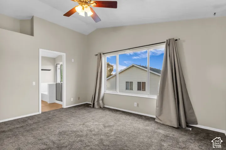 Vaulted ceiling with a ceiling fan, carpet flooring, and a large window with drapes