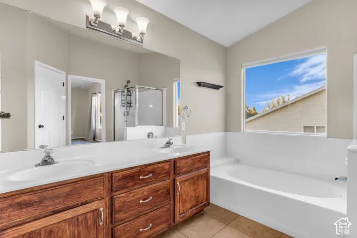 En suite bath with double vanity, wood-finish cabinetry, built-in soaking tub, and a separate glass-enclosed shower