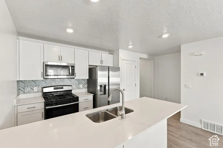 White cabinetry with stainless steel appliances, herringbone tile backsplash, white countertops, and wood-finish flooring