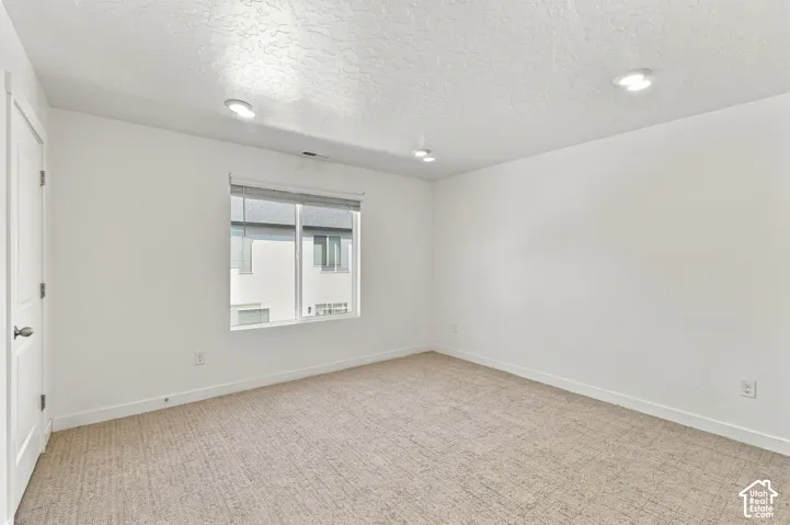 Recessed lighting, neutral-toned carpeting, window with blinds, white walls, and a white interior door