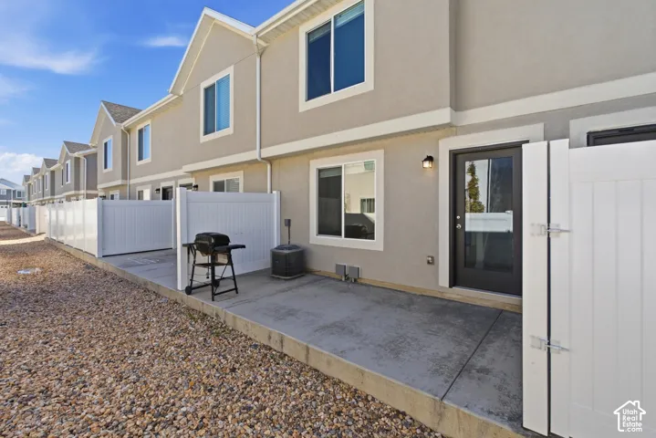 Private concrete patio with a full-light rear door, exterior lighting fixture, and white privacy fencing