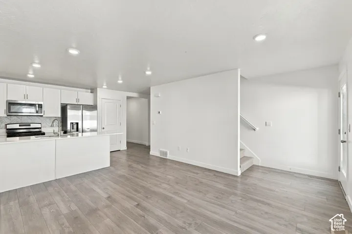 Open-concept layout featuring wood-finish flooring, recessed lighting, a modern kitchen with white cabinetry, stainless steel appliances, and a tiled backsplash