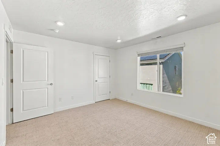 Neutral toned wall-to-wall carpeting, white walls, recessed lighting, and a large window with roller shades