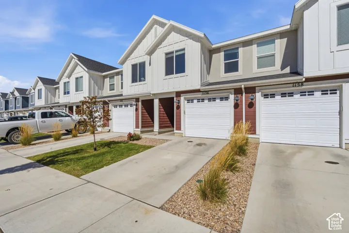 Contemporary townhome exterior featuring white siding, dark red accents, a dark shingle roof, and white garage doors