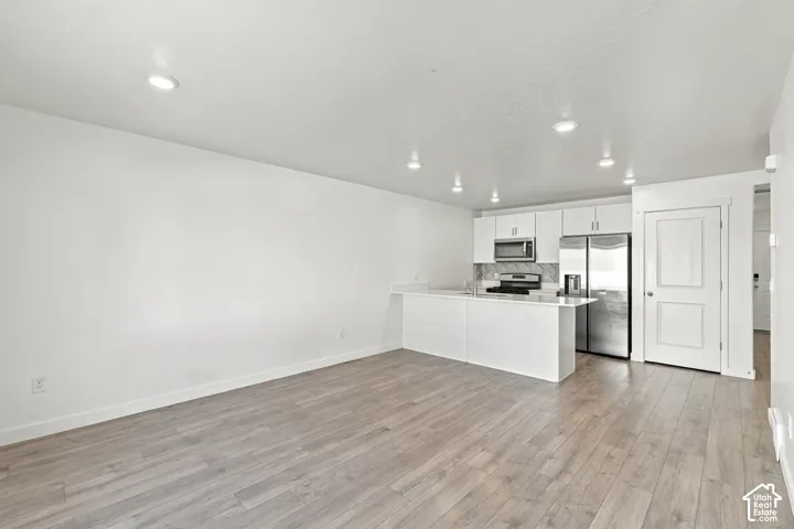 Open-concept living area featuring wood-finish flooring, recessed lighting, and a kitchen with white cabinetry, stainless steel appliances, and a breakfast bar
