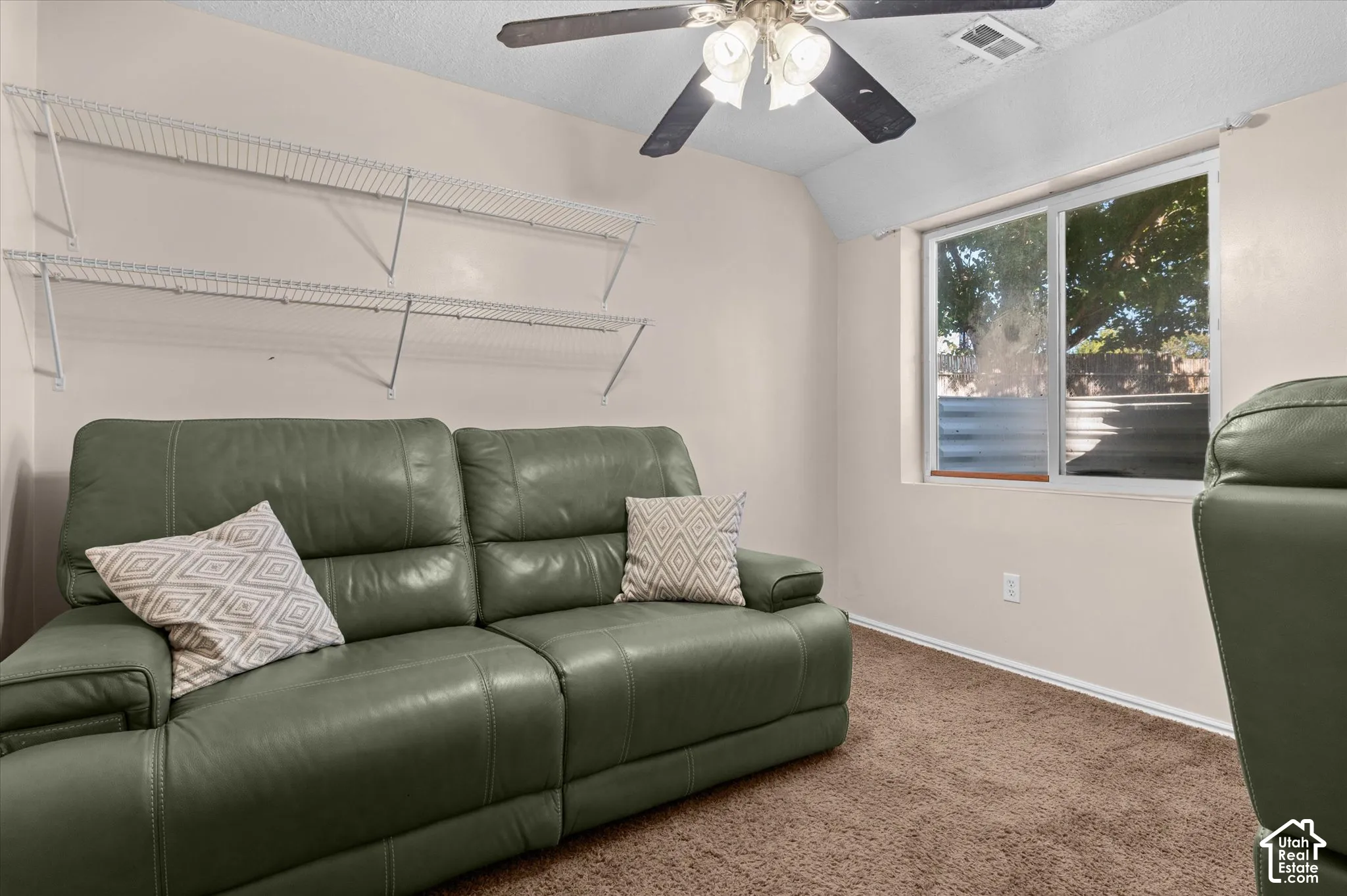 Carpeted flooring, white wire shelving, light-colored walls, ceiling fan with integrated lighting, and a window