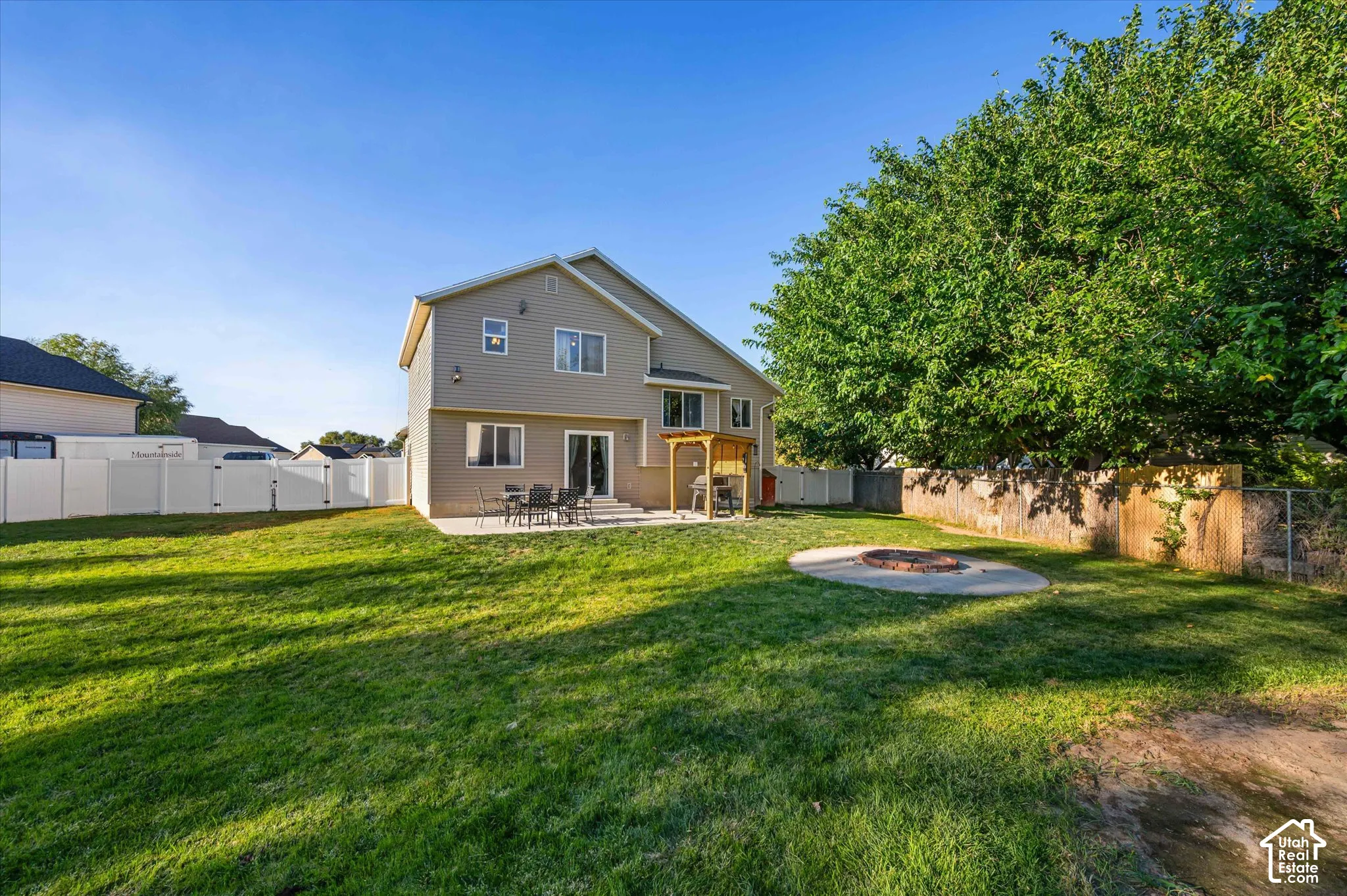 Expansive grassy yard with a concrete patio, a built-in fire pit, and a full privacy fence